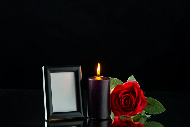 视图在黑暗的表面上有红玫瑰和画框的黑暗蜡烛的正面视图黑暗蜡烛燃烧