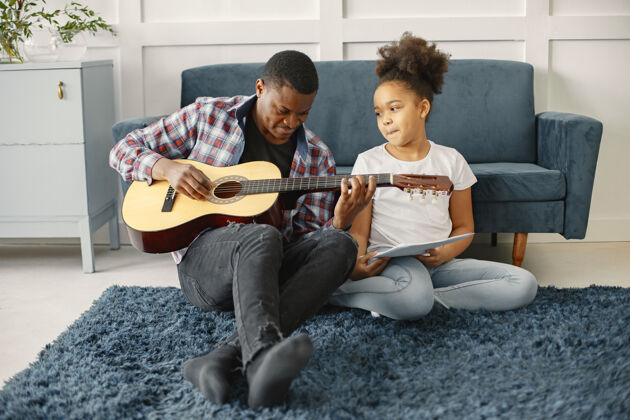 快乐父亲带着女儿坐在沙发上女孩拿着吉他学吉他情感地板关心