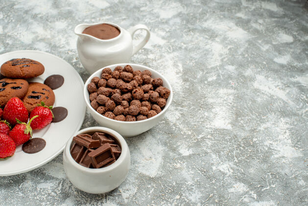 谷类食品下图：白色椭圆形盘子上的巧克力饼干草莓和圆形巧克力 灰白色地面左侧的碗里放着巧克力 麦片和可可盘子可可杯子