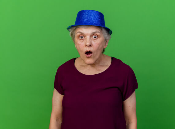 女人惊讶的戴着派对帽的老妇人看着绿色的摄像机派对老人惊喜
