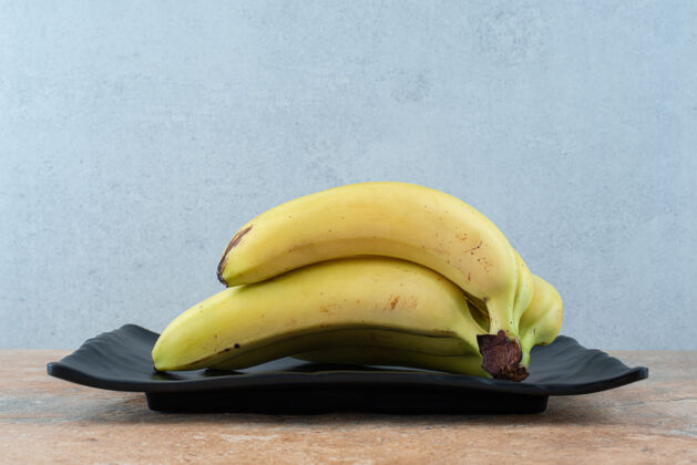 黄一个黑色的盘子里装满了成熟的水果香蕉 放在灰色的盘子里热带果皮香蕉