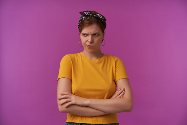 皱眉不高兴不满意的年轻女子穿着黄色T恤 头上戴着头巾 看起来很生气 双臂交叉在紫色的墙上沮丧女性失望