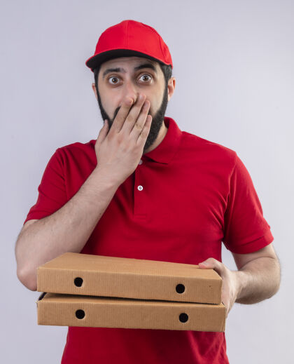 姿势年轻帅气的送货员穿着红色制服 戴着帽子 手里拿着披萨盒 手放在隔离在白色墙上的嘴上人送货感觉