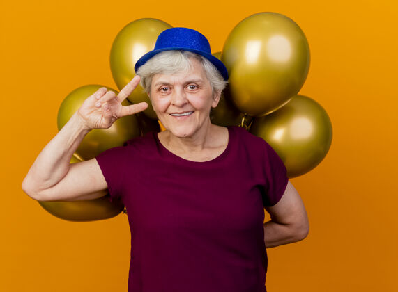 胜利面带微笑的老妇人戴着聚会帽 打着胜利手势 手里拿着氦气球老人微笑穿