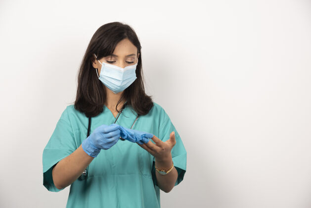 职业戴着医用口罩的女医生看着白色背景上的手套高质量的照片听诊器女性医疗
