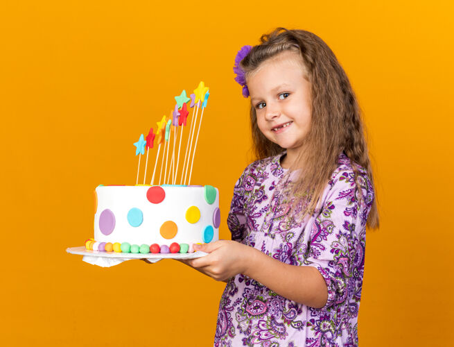 孤立带着微笑的金发小女孩拿着生日蛋糕隔离在橙色的墙上 有复制空间微笑蛋糕女孩