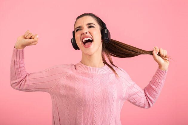 耳机戴着无线耳机听音乐的年轻女子穿着粉色毛衣微笑着摆出粉色的姿势设备无线立体声