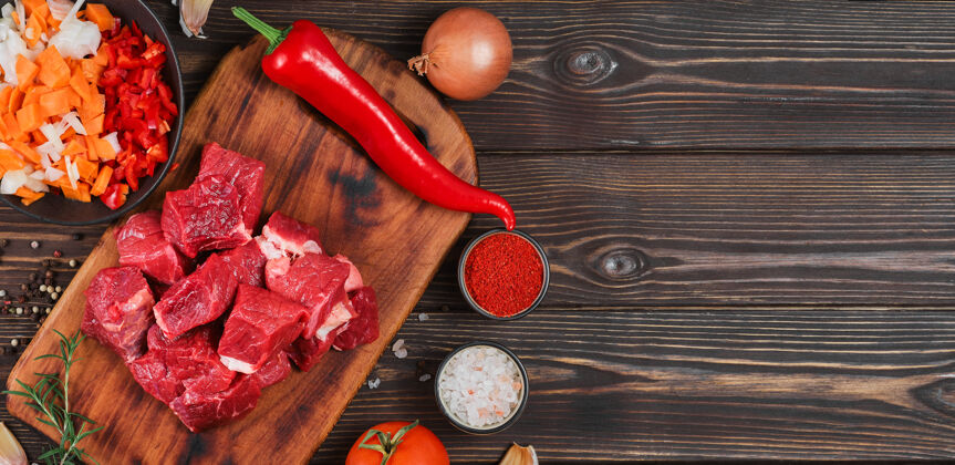 牛肉制作意大利炖肉或炖肉 炖肉或绞肉的原料黑木桌上的生牛肉 香草 香料 辣椒粉 蔬菜的俯视图服务番茄块