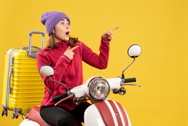 抱前视图坐在轻便摩托车上的年轻女子指着什么东西成人快乐前面