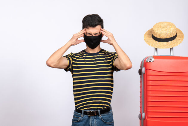 休闲正面图疲惫的年轻游客戴着黑色面具站在红色手提箱旁视图人姿势