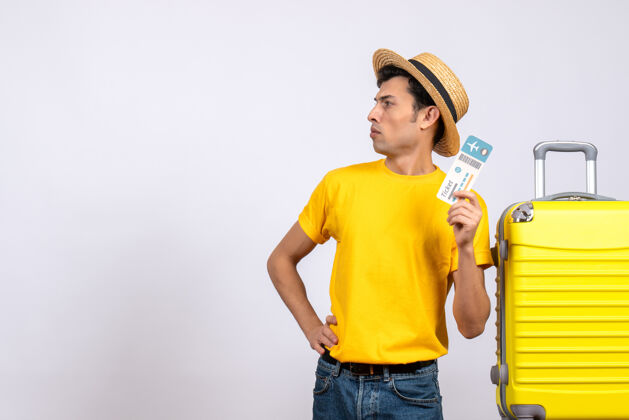 腰部正面图穿着黄色t恤的年轻人站在黄色手提箱旁 手放在腰上视图休闲成人