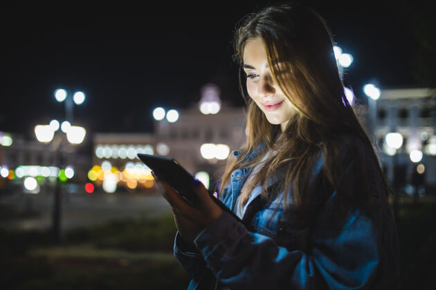 聊天年轻快乐的女人用平板电脑在户外模糊的夜晚城市灯光夜晚休闲街道