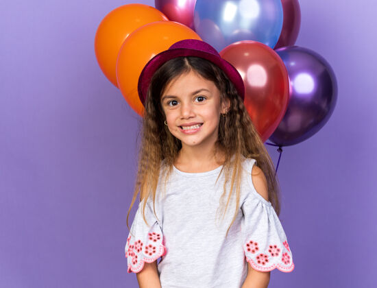 白种人带着紫色派对帽微笑的白人小女孩站在紫色墙上 氦气球与复制空间隔离生日气球微笑