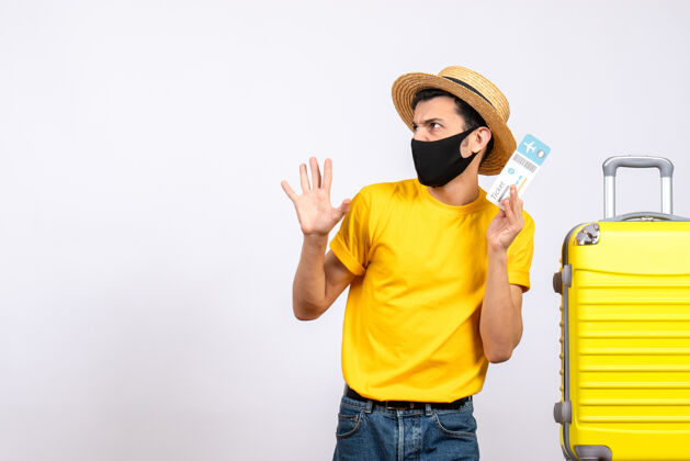 年轻人正面图：戴草帽的年轻人站在黄色手提箱旁 手里拿着机票黄色持有休闲