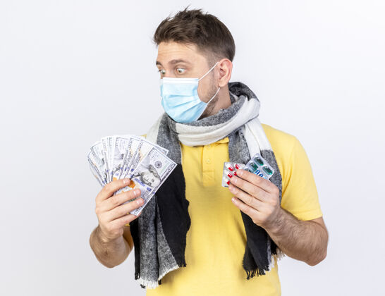 围巾一个戴着医用面罩和围巾的年轻金发病患 手里拿着钱和几包药片 隔离在白墙上人市民药片