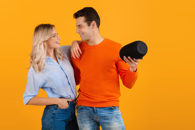 积极美丽的微笑着的年轻夫妇手持无线扬声器听音乐的橙色情侣乐趣科技