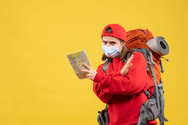 背包正面图：年轻的女性徒步旅行者背着背包 戴着面具 手拿地图快乐成人面具