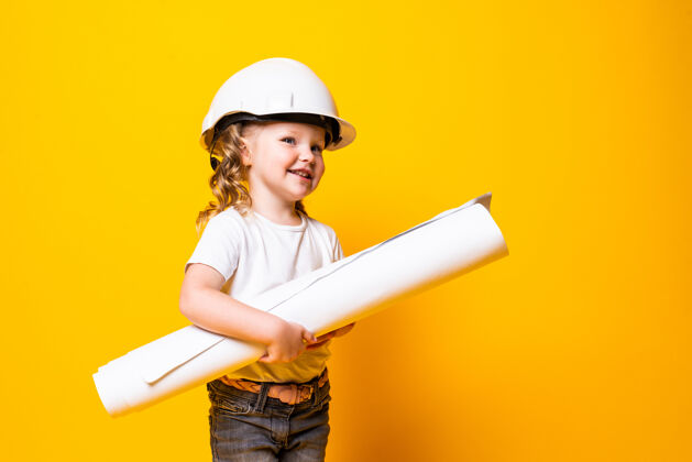 孩子可爱的小女孩工程师 戴着头盔 把蓝弹簧隔离在黄色的墙上年轻绘画可爱