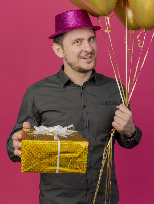 气球高兴的年轻人戴着粉红色的帽子拿着气球和礼品盒孤立的粉红色派对戴着帽子