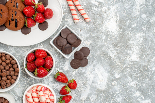 壁板顶视图饼干草莓和圆形巧克力在椭圆形盘子碗糖果草莓巧克力谷类食品在灰白色的桌子左侧碗草莓椭圆形