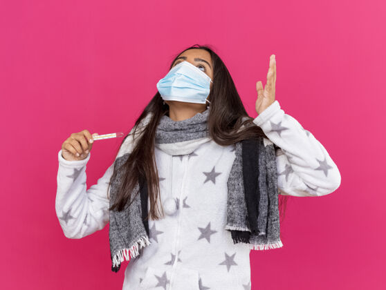 累疲惫的生病少女戴着医用面罩 戴着围巾 手举温度计 手上隔离着粉色口罩粉色医疗