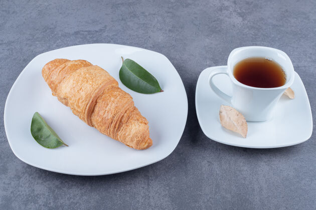 面包新鲜的法式牛角包配上一杯茶和一块金色的面包皮烹饪面粉糕点