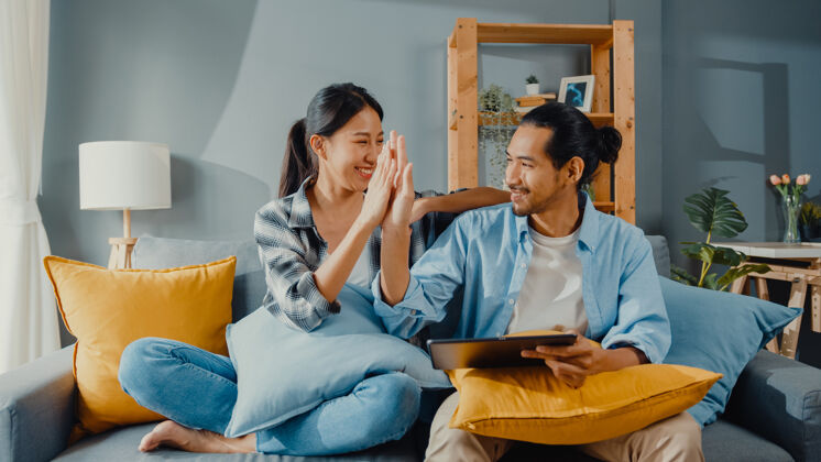亚洲快乐的亚洲年轻漂亮的夫妇男女坐在沙发上用平板电脑在新房子里在线购买家具公寓笑在线