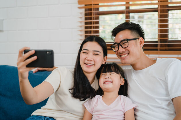 技术快乐快乐的亚洲家庭爸爸 妈妈和孩子们在家里的沙发上玩得开心 使用智能手机视频通话距离房子电话
