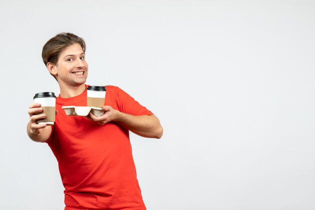男人正面图是一个微笑的年轻人 穿着红色上衣 在白色背景下拿着纸杯里的咖啡纸张年轻人人物