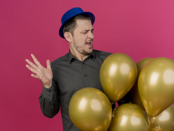 帽子一个戴着蓝色帽子的年轻人拿着气球 看着粉红色的气球派对戴着年轻