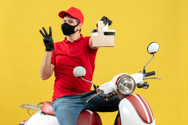 男人前视图自信的信使男子穿着红色上衣 戴着帽子手套 戴着医用面罩 坐在摩托车上拿着三张订单车辆帽子医疗