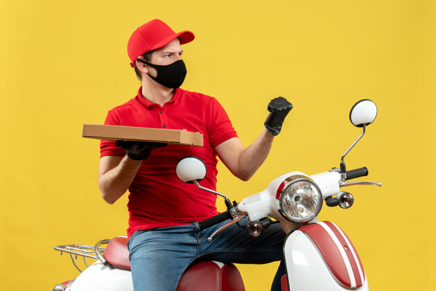 男子俯视图：情绪高昂 野心勃勃的快递员身穿红色上衣 戴着帽子手套 戴着医用面罩 坐在滑板车上显示秩序手套头盔摩托车