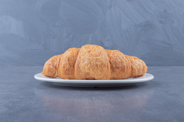 餐桌白盘子上的新鲜法式牛角面包对象黄油填充