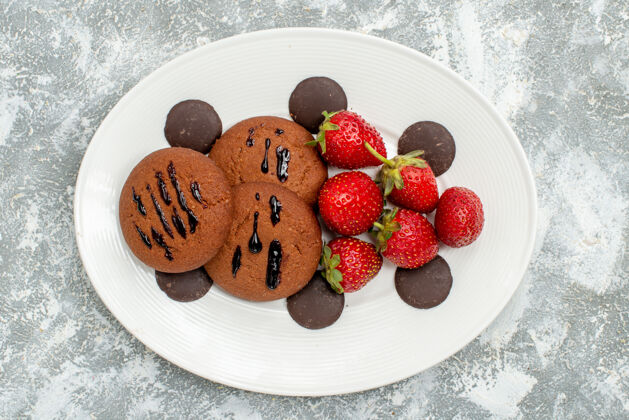 草莓顶近距离观看巧克力饼干草莓和圆形巧克力在白色椭圆形盘子上的灰白色地面饮食磨碎椭圆形