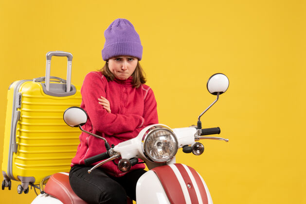 手前视图闷闷不乐的年轻女子骑着轻便摩托车双手交叉坐着摩托车椅子