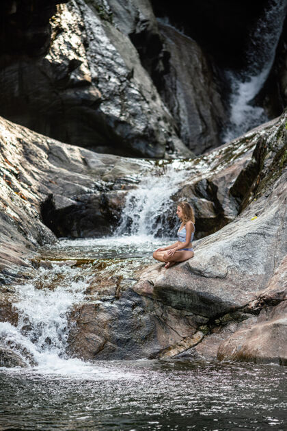成人一位女性在瀑布附近冥想的垂直镜头和谐身体放松