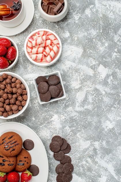 巧克力左上角是饼干草莓和圆形巧克力放在椭圆形的盘子里 糖果草莓和巧克力麦片和一杯茶放在灰白色的桌子上食物香料糖果