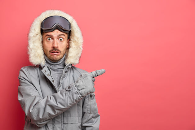 男照片中 一个情绪激动的欧洲男人穿着冬装 戴着滑雪镜 指着右边空白处的方向穿季节外套