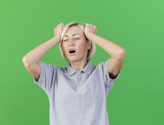 疾病疼痛的年轻金发病斯拉夫妇女把手放在头上隔离在绿色墙壁与复制空间头疼痛年轻