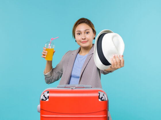 前面正面图：度假中的女性手持新鲜果汁和浅蓝色背景上的帽子远航海上度假之旅蓝色旅行假期