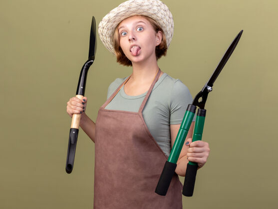 斯拉夫年轻的斯拉夫女园丁戴着园艺帽 拿着铲子和园艺剪刀在橄榄绿上跺着舌头园艺橄榄印象