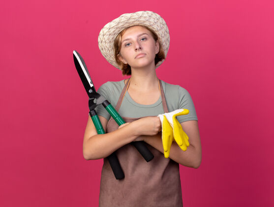 年轻自信的年轻斯拉夫女园丁戴着园艺帽拿着园艺剪刀和粉色手套帽子女剪刀