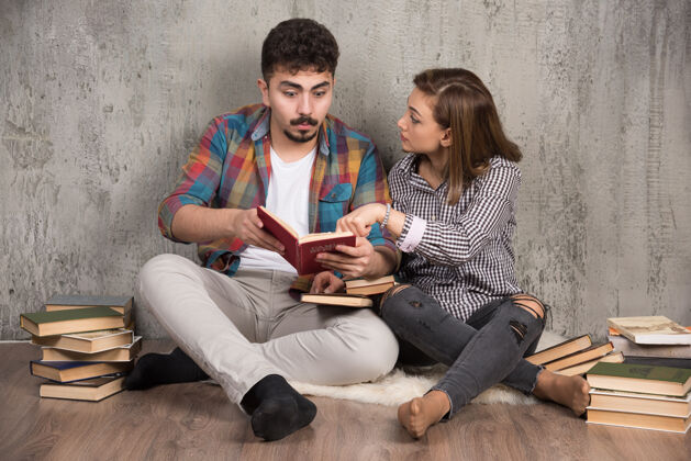 女人一对年轻夫妇坐在地板上看一本有趣的书讨论乐趣举行