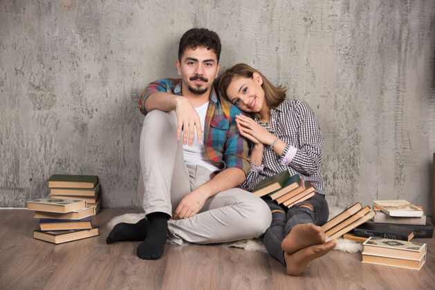 阅读坐在地板上拿着书微笑着的年轻夫妇美丽快乐地板