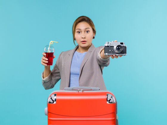 微笑前视图：度假中的女性拿着果汁和相机在淡蓝色的背景上旅行度假旅行海上飞机前面航行旅行
