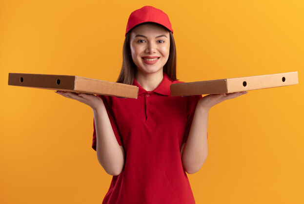 手身着制服 面带微笑的漂亮送货员手里拿着披萨盒 手里拿着橘色的送货橘子制服