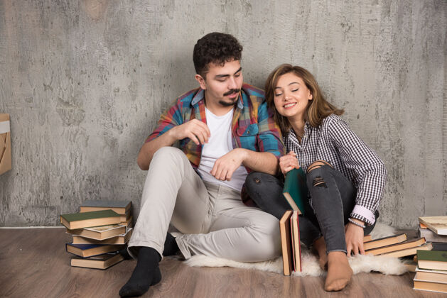 模特坐在地板上拿着书的年轻夫妇地板情侣坐着