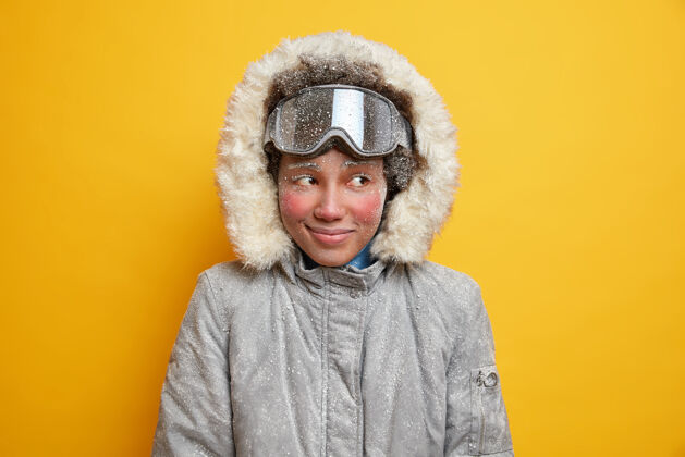 雪梦幻的冬日女孩 冻红了脸 在寒冷的大雪天享受着度假胜地的乐趣 雪片覆盖着 穿着暖和的夹克 戴着风帽 戴着滑雪镜 喜欢极限运动大笑封面外套