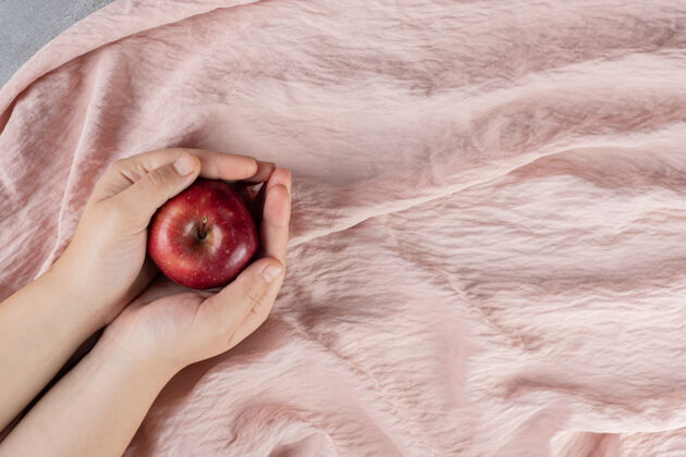 杯子双手抱着一个苹果在织物表面膳食饮食食物