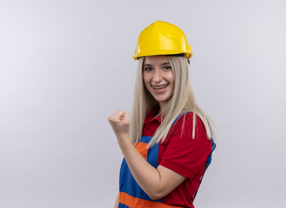 太空微笑着的年轻金发工程师建筑工女孩穿着制服戴着牙套举起拳头在孤立的空白空间与复制空间微笑金发女孩